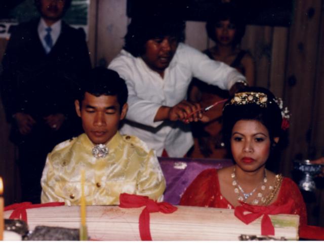 In this photo, the bride’s hair is symbolically cut in the Kat Sak (Hair cutting) wedding ceremony to represent a fresh start. Relatives and friends take turns cutting the hair of the bride and groom to cleanse the couple in preparation for their new life together and to bestow blessings of good fortune, happiness, prosperity, and longevity.