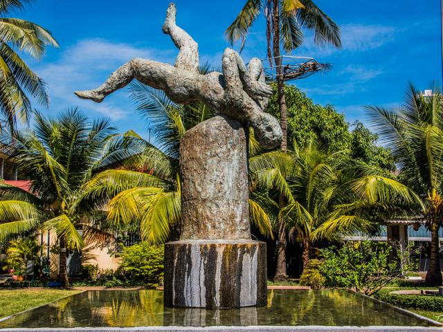 "This sculpture is in the central courtyard at Tuol Sleng Genocide Museum is part of a memorial entitled ""For Those Who Are No Longer Here"" by French-Cambodian artist Séra Ing  The sculpture is one of the reparations projects outlined in the 2014 judgment handed down by the Khmer Rouge tribunal in Case 002/01 against former Brother Number Two Nuon Chea and former head of state Khieu Samphan.  The work, a mottled bronze figure frozen mid-air as it tumbles backwards with its hands pressed into a sampeah, ev