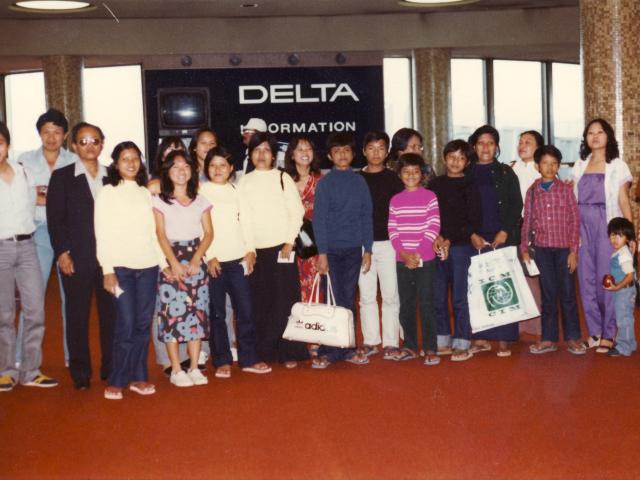 The Kem family is greeted at the airport in San Francisco. The bag held by Mrs. Kim (on the right) contains all of the families travel documents. Her son (in center of photo) is holding the only personal possessions the family had when they arrived. After their arrival in San Francisco, the family moved to the Long Beach area (circa 1980).