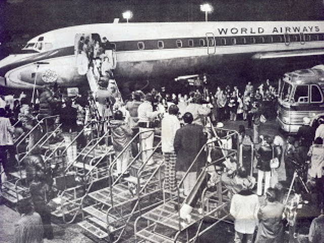 4/2/1975 The East side of Hangar 110, Oakland International Airport as Members of the press and others meeting the first “un-official” flight of Vietnamese orphans. The bus seen in the picture was one of several that transported the arriving orphans to the Armory at the San Francisco Presidio.