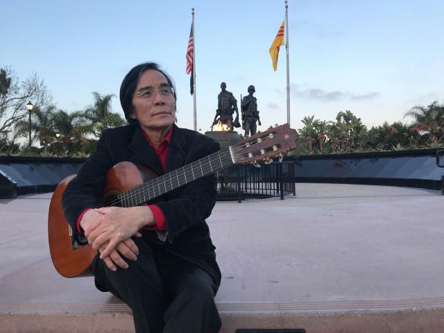 Famous composer Trần Chí Phúc, known for his work on “refugee music,” stands next to the Vietnam War Memorial in Liberty Park, Westminster, CA.