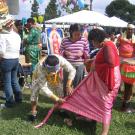 Performers help each other get dressed for their performances at Cambodian New Year in Long Beach. The woman is being helped with her kbun. An 8’ length of silk is wrapped around her waist toward the front. The length of cloth will be twisted and pulled to her back between her legs. It is held in place with a belt.