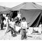 Photograph of a woman and children outside a tent.